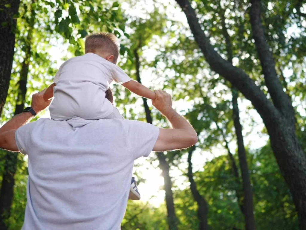 father letting kid sit on his shoulders through the woods