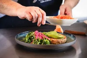 A chef plating avocado toast with smoked salmon and greens